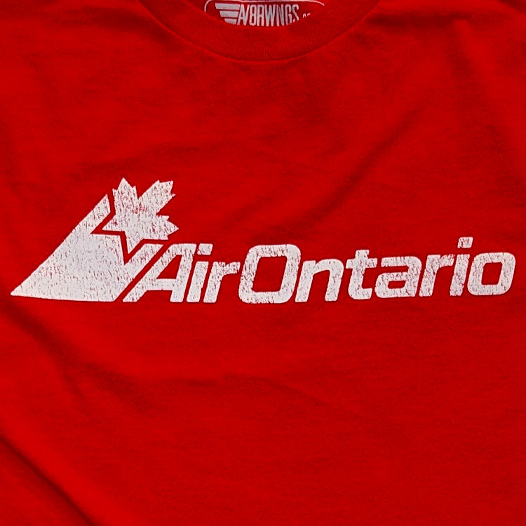 A close-up of a red t-shirt featuring a distressed white graphic of a mountain with a maple leaf and the text 'Air Ontario'. The inner collar shows the brand name 'AV8R Wings'.