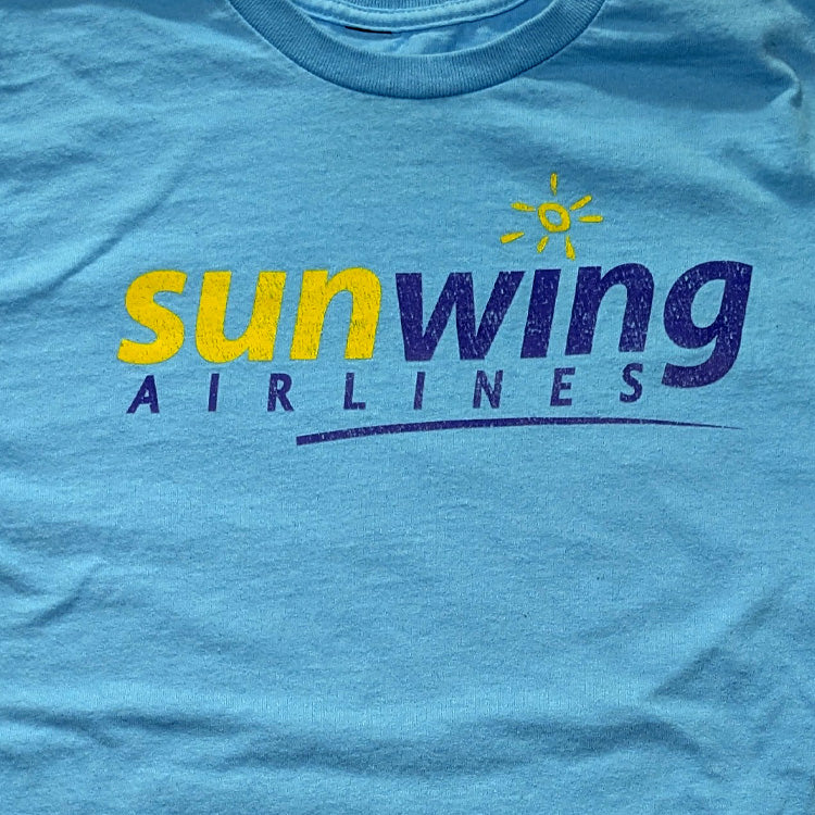 A close-up of a light blue t-shirt featuring a distressed graphic print of the 'sunwing AIRLINES' logo in yellow and dark blue, with a small yellow sun icon above the text.